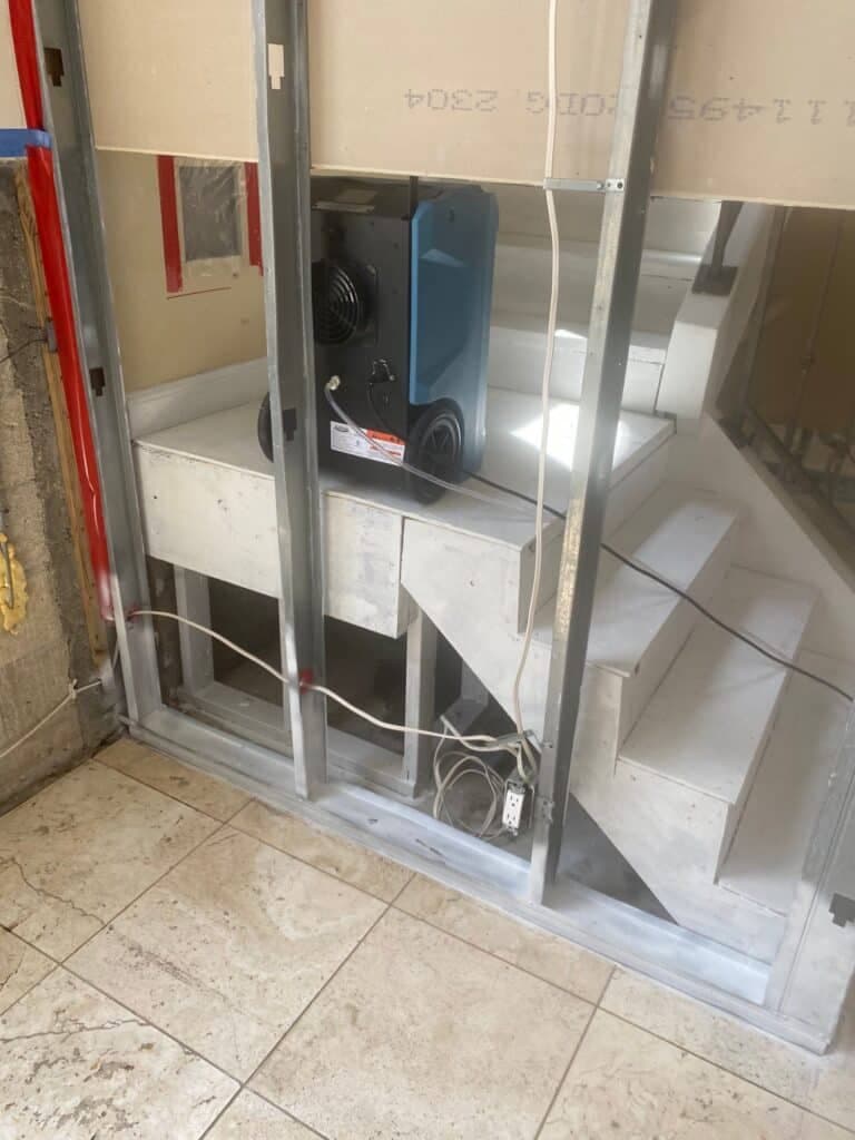 Structural drying equipment running behind an opened wall and staircase on a TLG Restoration flood recovery job